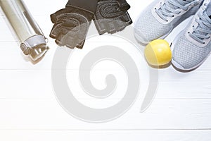 Sport photo. Healthy lifestyle. Bottle for water, apple and leather gloves. Stylish trainers. White wooden background. Perfect