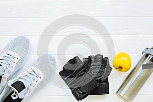 Sport photo. Healthy lifestyle. Bottle for water, apple and leather gloves. Stylish trainers. White wooden background. Perfect