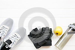 Sport photo. Healthy lifestyle. Bottle for water, apple and leather gloves. Stylish trainers. White wooden background. Perfect