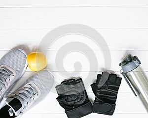 Sport photo. Healthy lifestyle. Bottle for water, apple and leather gloves. Stylish trainers. White wooden background. Perfect