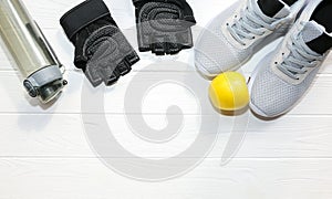 Sport photo. Healthy lifestyle. Bottle for water, apple and leather gloves. Stylish trainers. White wooden background. Perfect