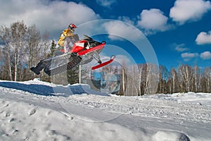 Sport red snowmobile jump. Sunny winter day with blue sky. Concept quick movement. photo