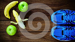 Sport shoes, apples and bananas on a wooden background. Sport