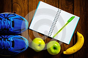 Sport shoes, apples and bananas on a wooden background. Sport