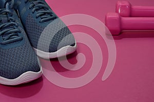 Sport sneakers and dumbbells on pink background with copy space for text. Sport objects background. Sports concept