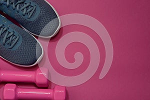 Sport sneakers and dumbbells on pink background with copy space for text. Sport objects background. Sports concept