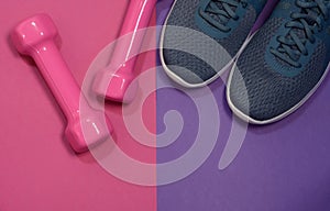 Sport sneakers and womens dumbbells on pink purple background with copy space for text. Sport objects background. Sports concept