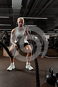 Sport. Strong man exercising with battle ropes at the gym with. Athlete doing battle rope workout at gym. Dramatic