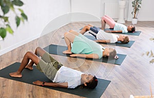 In sport studio with group of friends, African boy perform bridge pose, setu bandha sarvangasana