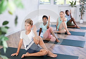 In sport studio with group of friends, boy perform Lord of Fishes asana, Ardha Matsyendrasana