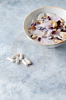 Sport supplements carnitine capsules and bowl of granola with yogurt, nuts, cranberry and cocoanut in background.