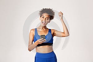 Sport and technology concept. Attractive african-american female athelte achieve goal in worout app, holding smartphone