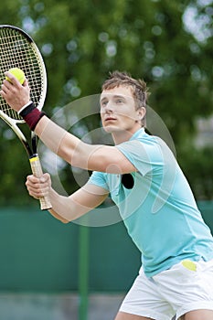 Sport and Tennis Concept: Handsome Caucasian Man With Tennis Raquet Preparing to Serve Ball On Court