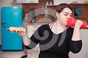 Sport with unhealthy food. combination of active life with fast food. close up photo. fat woman choosing dumbbell not hamburger