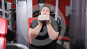 Sport with unhealthy food. Young plus size fat woman puts away barbells and takes a large cake. Young woman looking