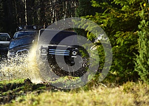 Sport utility vehicle or SUV crossing puddle with splash. Offroad race on fall nature background. Rallying, competition