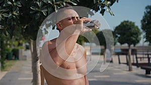 Sport and water balance concept. Close up portrait of young sporty man drinking water from bottle during jog training at