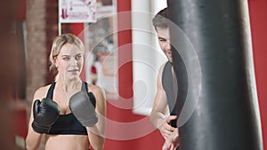 Sport woman boxing punching bag in gym club with personal trainer.