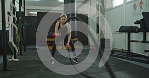 Sport woman doing battle ropes exercise at gym. Fitness girl athlete with fit body exercising, doing functional training