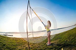 Sport woman doing  training outdoors with TRX at daytime. Total body resistance exercises for her healhty lifestyle