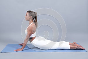 Sport woman in downward facing dog yoga pose. Beautiful girl working out on gray background, doing yoga exercise, adho