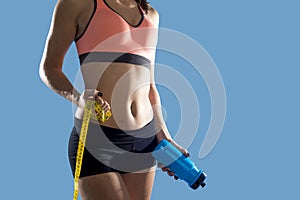 Sport woman holding water bottle and measure tape showing slim perfect abs and stomach