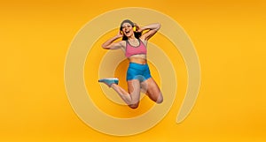 Sport woman jumps on a yellow background and listen to music. Happy and joyful expression.