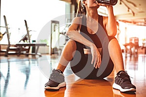 Sport woman relax resting after workout or exercise in fitness gym. Sitting and drinking protein shake or drinking water on floor