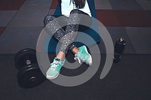 Sport woman sitting and resting after workout or exercise in fitness gym with protein shake or drinking water on floor