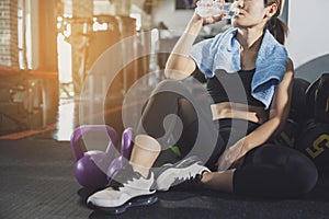 Sport woman sitting and resting after workout or exercise in fitness gym with protein shake or drinking water on floor. Relax