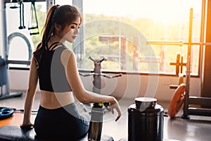 Sport woman sitting and resting after workout or exercise in fitness gym with protein shake or drinking water on floor. Relax