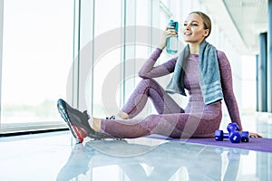 Sport woman sitting and resting after workout or exercise in fitness gym with protein shake or drinking water on floor. Relax