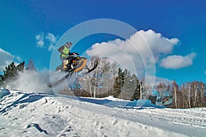 Sport yellow snowmobile jump. Sunny winter day with blue sky. Concept quick movement. photo
