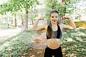 Sport young woman with perfect body showing biceps, fitness girl in green park