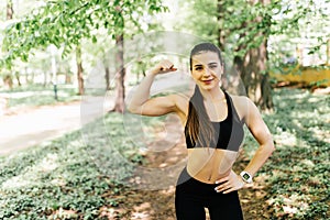 Sport young woman with perfect body showing biceps, fitness girl in green park