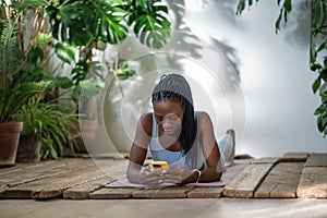 Sported black woman use smartphone take break from workout yoga, rest with smartphone on fitness mat