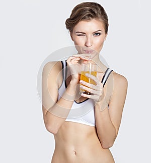 Sporting a beautiful young smiling girl with a glass of orange juice in his hands winks, healthy living, photography Studio