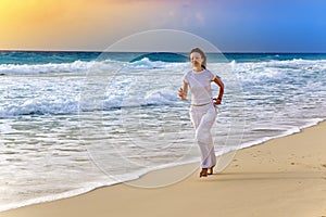 Sporting woman run on the sea coast on a beach on a sunset