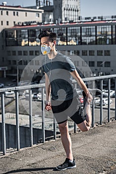 sportive asian teenager stretching in protective mask on bridge air