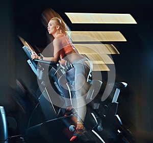 Sportive blonde woman working out on an exercise bike in modern fitness center. Fitness lifestyle in sport club.