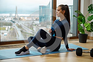 Sportive brunette with water bottle in hand sits on mat