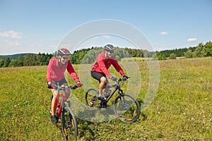 Sportive couple riding bike in summer meadow