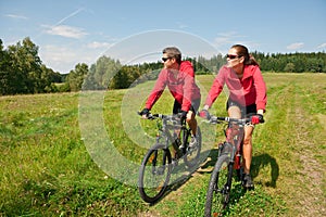 Sportive couple riding bike in summer meadow