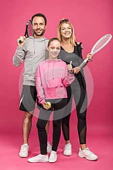 sportive family holding tennis rackets and ball, while child showing thumb up, isolated
