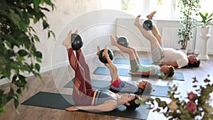 Sportive family members engaged in pilates lying on the floor on black mat holding softball between legs