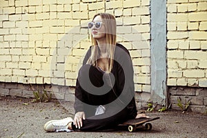 Sportive fashion woman sitting on skateboard. Young Girl in sunglasses with longboard on city streets
