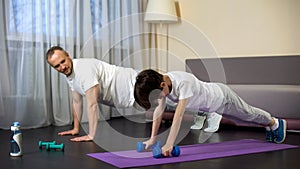 Sportive father teaching his son doing push-ups, military training, endurance