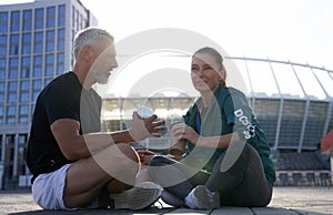 Sportive fit couple having conversation while sitting outdoors after morning workout on a sunny summer day