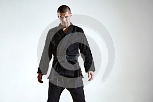 Sportive frowning man in black kimono for karate or kudo on white studio background with copy space