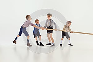 Sportive game. Group of little boys, children playing together, pulling the rope over grey studio background. Concept of